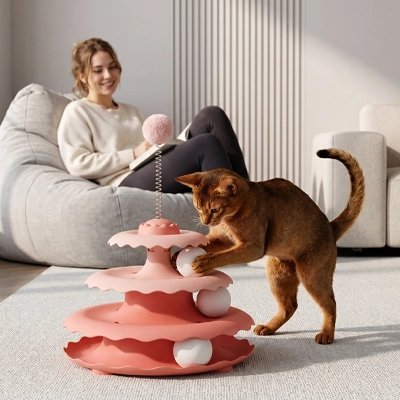  chat brun debout touchant une balle blanche dans une tour de jeu rose à trois niveaux
